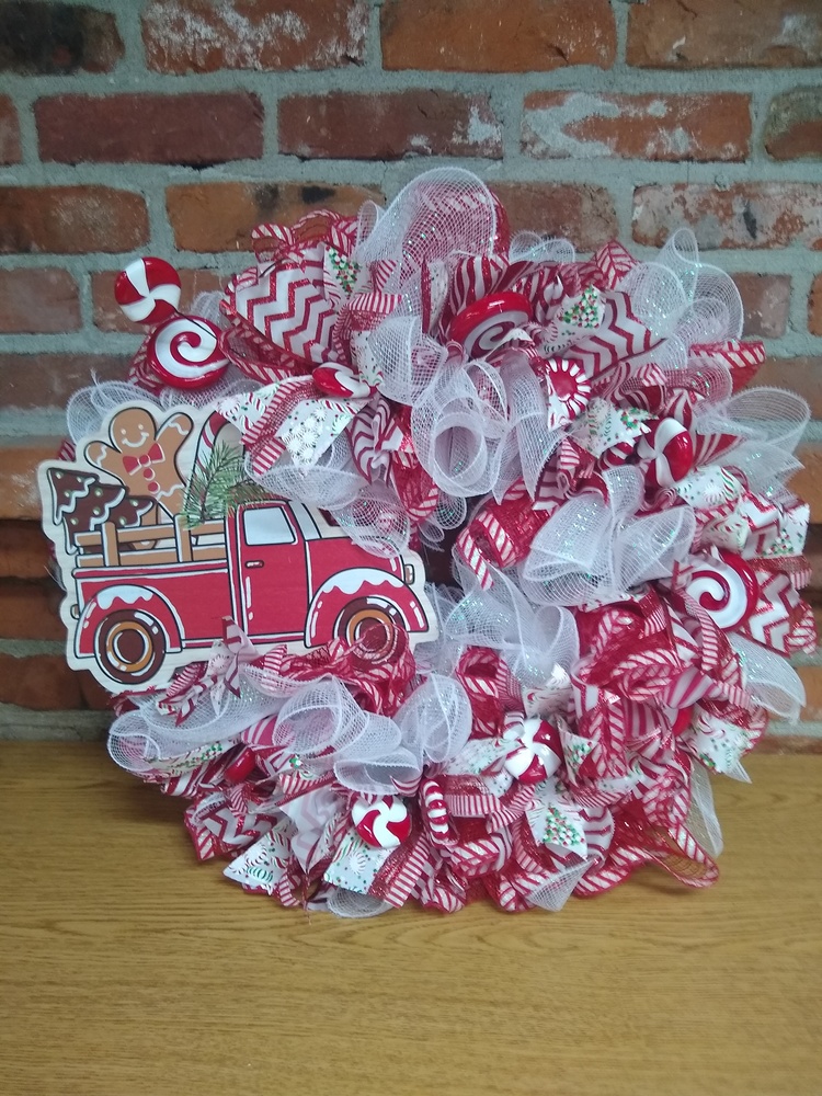 holiday ribbon wreath. A truck with a gingerbread man is the centerpiece. The wreath is made of white and red ribbon.